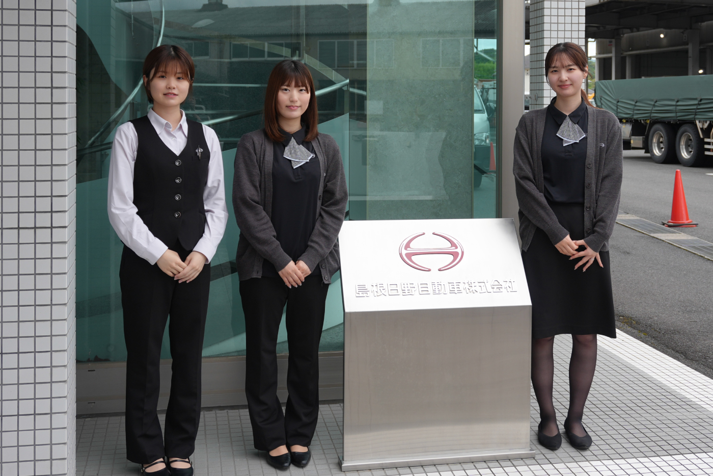 自動車会社で働く女性スタッフ3名が事務服着て立っている写真
