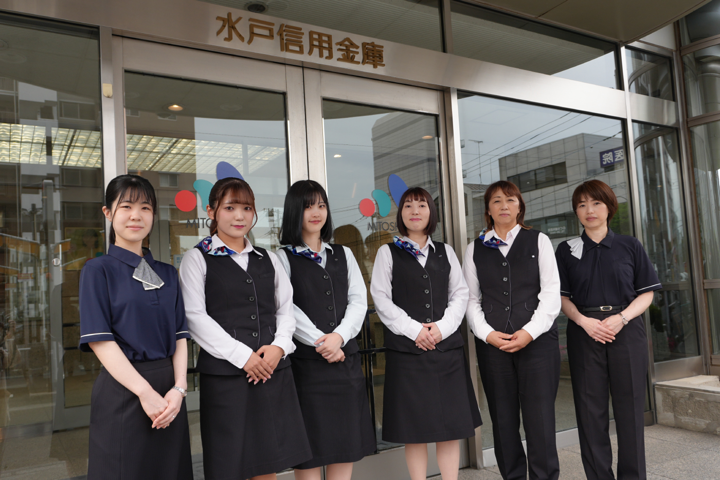 水戸信用金庫の前に事務服を着た女性6名が立っている画像