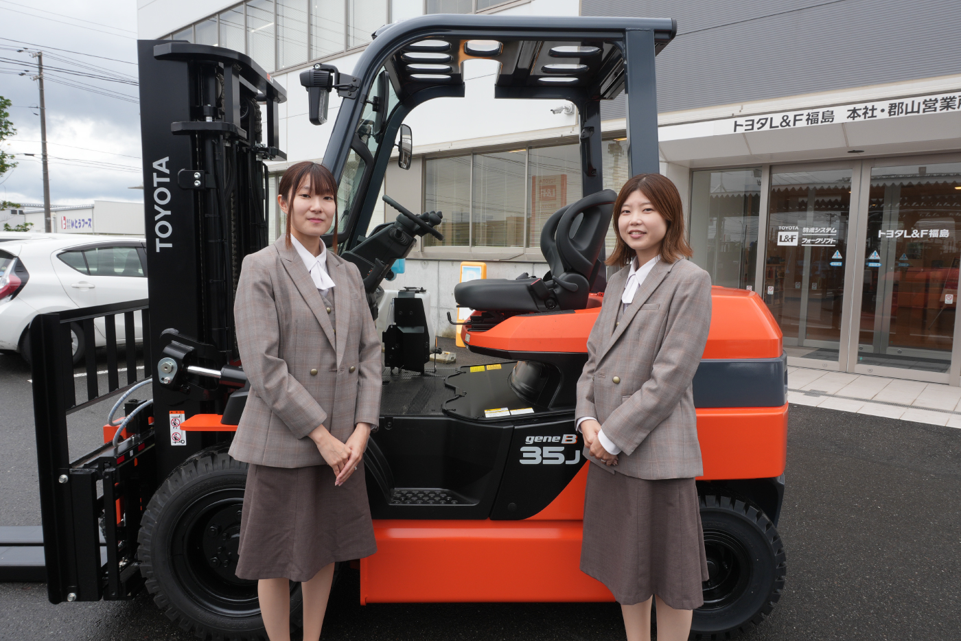 フォークリフトの前でユニフォームを着た女性スタッフ2名が立っている写真。